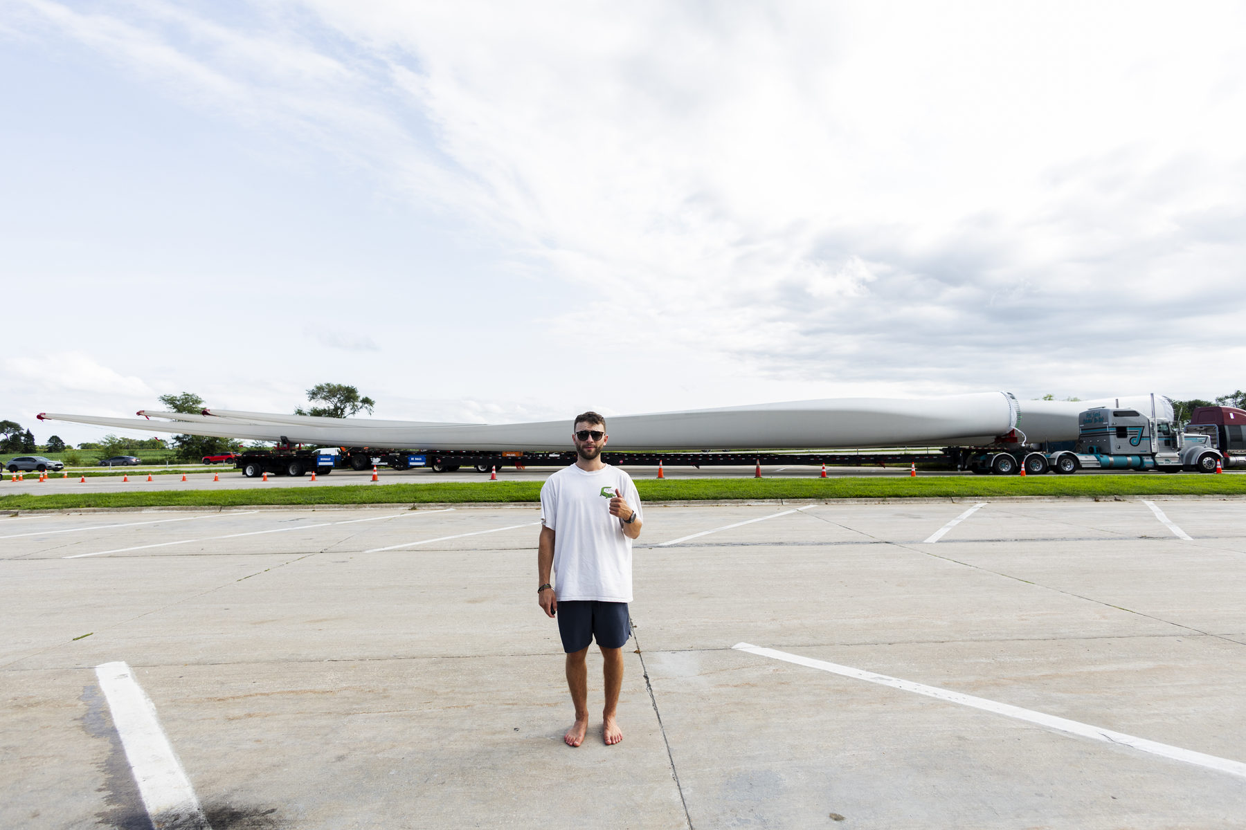 Thumbs up in a parking lot beside a massive wind turbine blade in Iowa